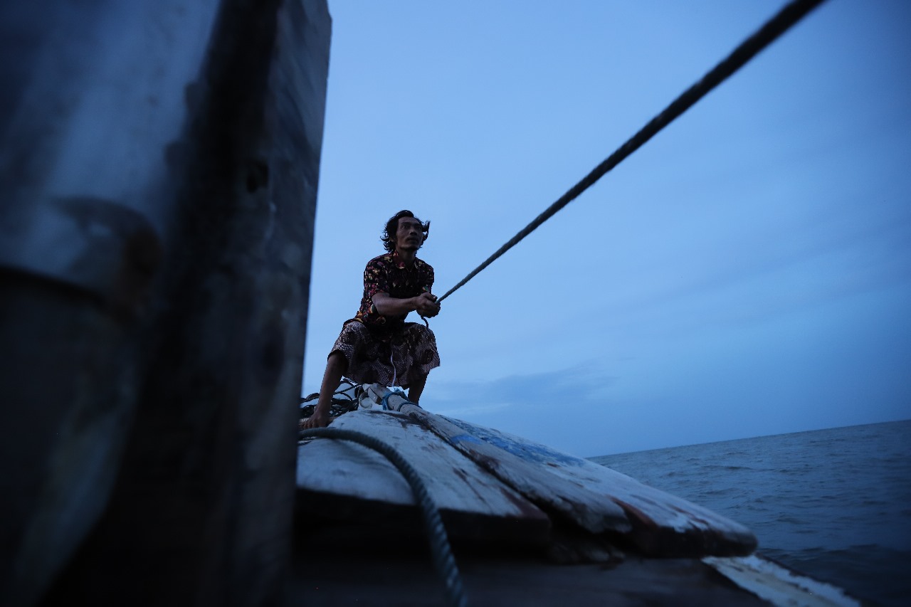 Nelayan Menarik tali jangkar diatas kapal yang perlahan melaju
